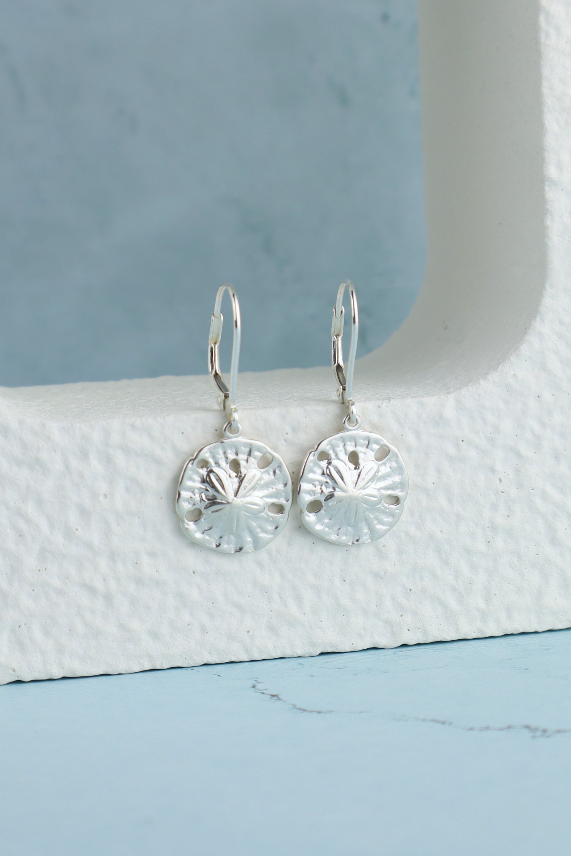 Silver sand dollar earrings on a white stand with a light blue background