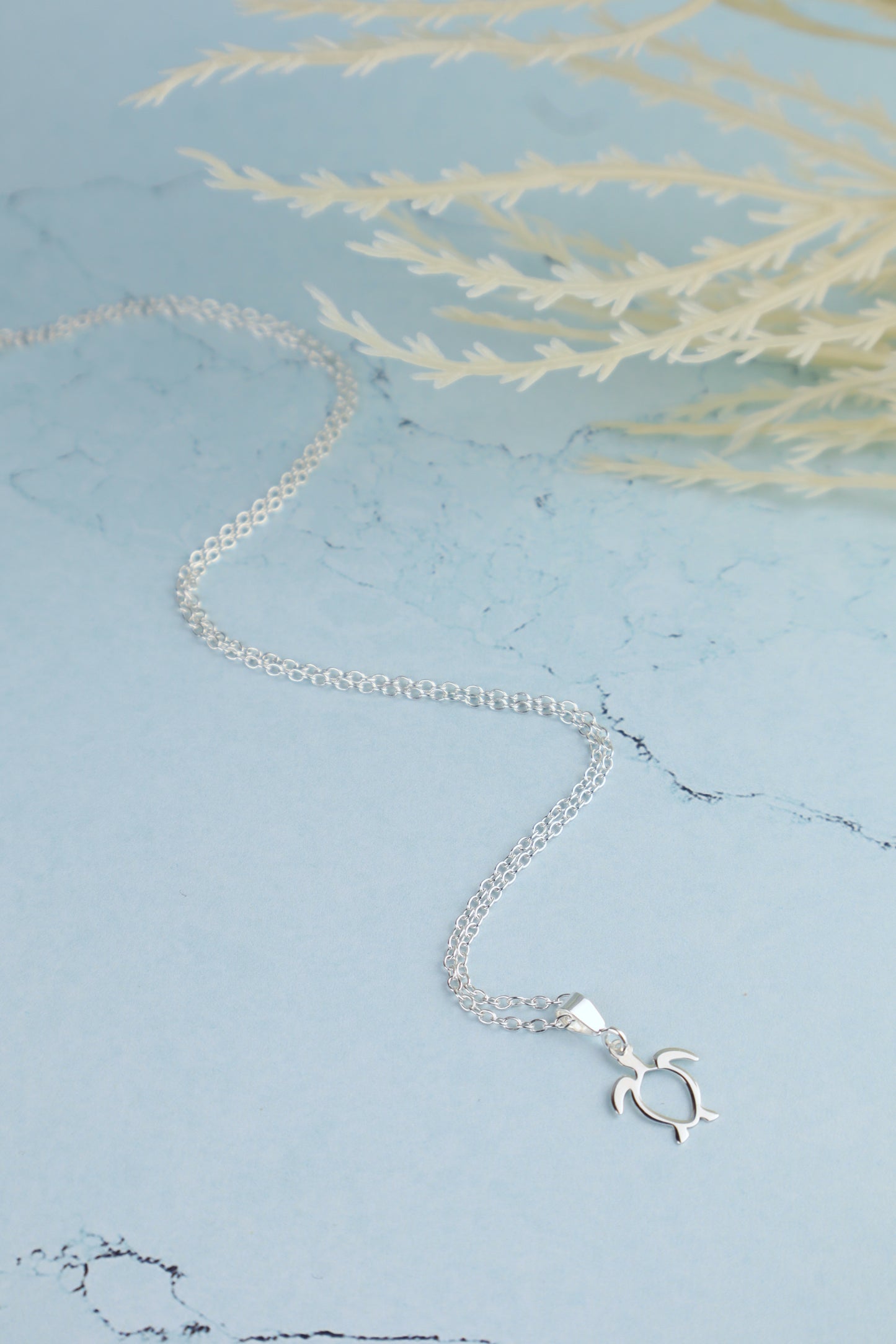 sterling silver sea turtle necklace for women laying on a marble blue background