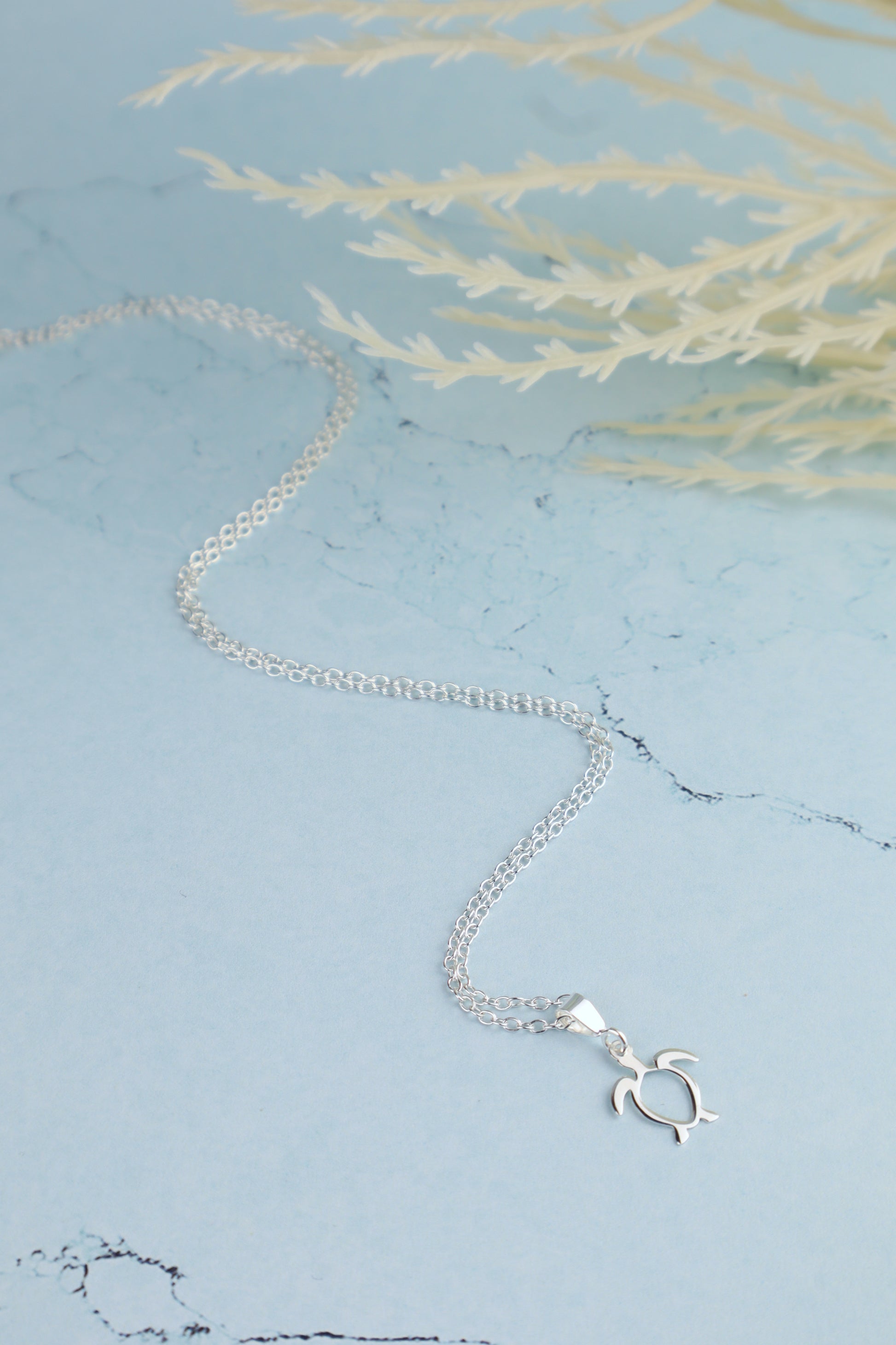 sterling silver sea turtle necklace for women laying on a marble blue background