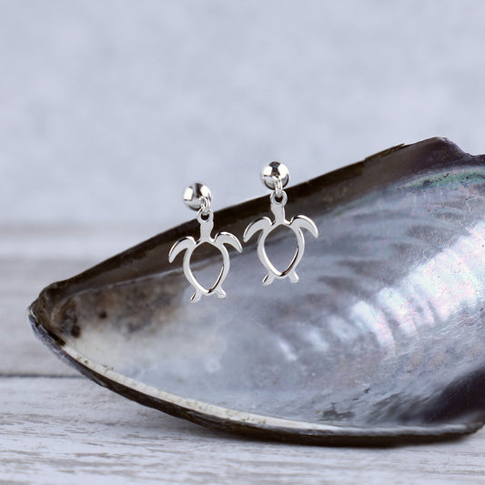 Silver turtle-shaped earrings on a shell with a gray background