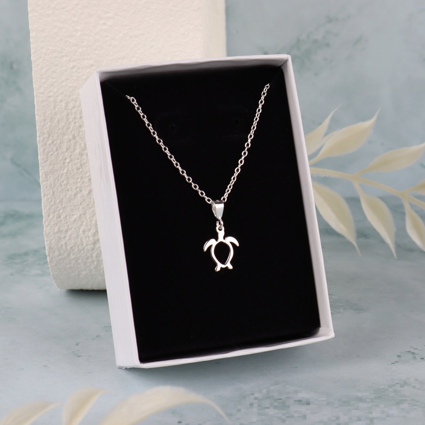 Silver turtle pendant necklace in a black box on a light blue background