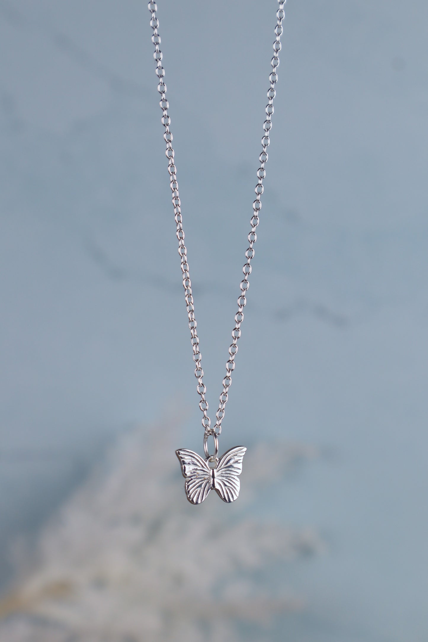 sterling silver butterfly pendant necklace hanging Infront of a blue background