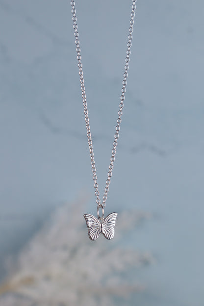 sterling silver butterfly pendant necklace hanging Infront of a blue background