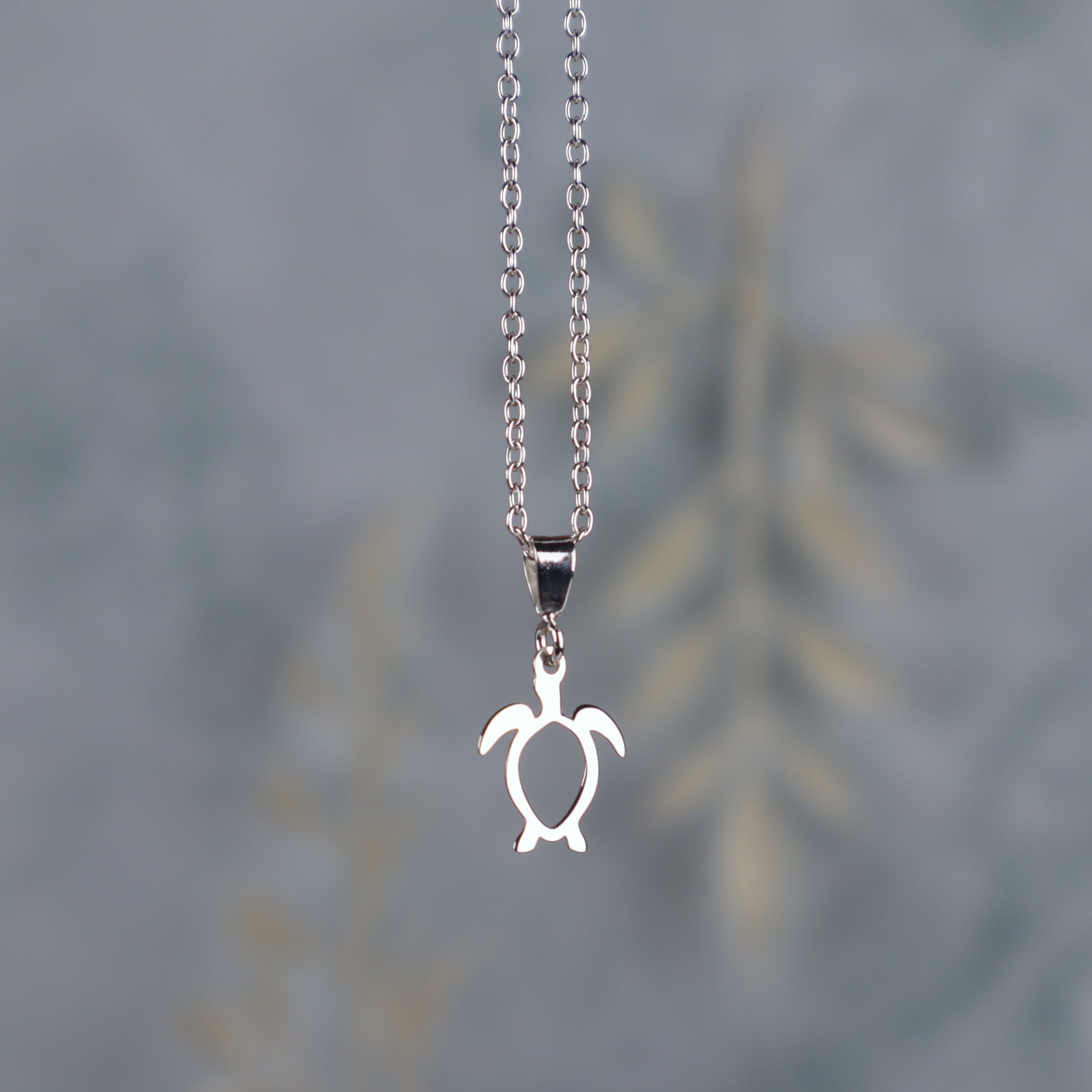 sterling silver sea turtle necklace for women hanging in front of a blue background with leaves