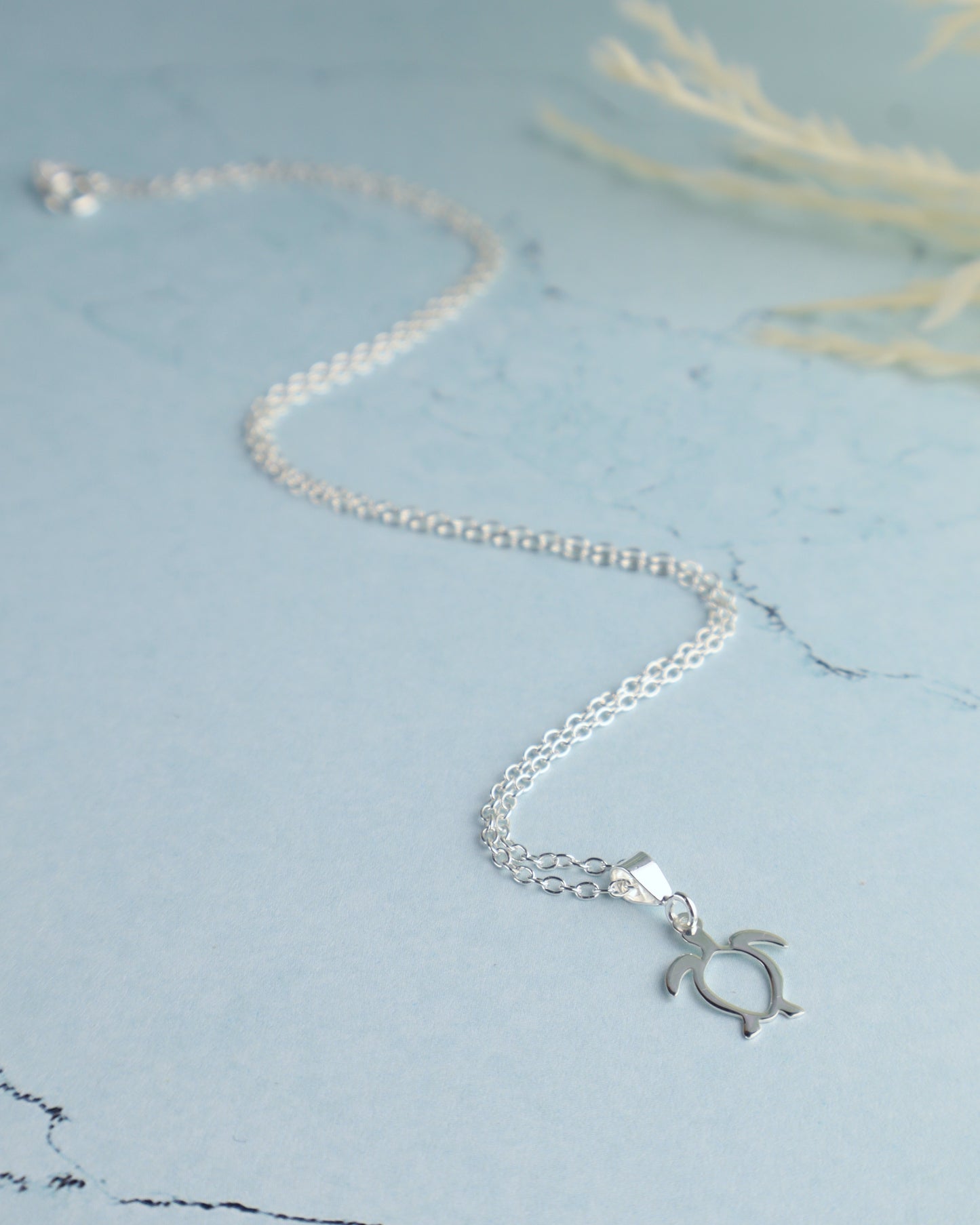 sterling silver sea turtle necklace for women resting on a blue background