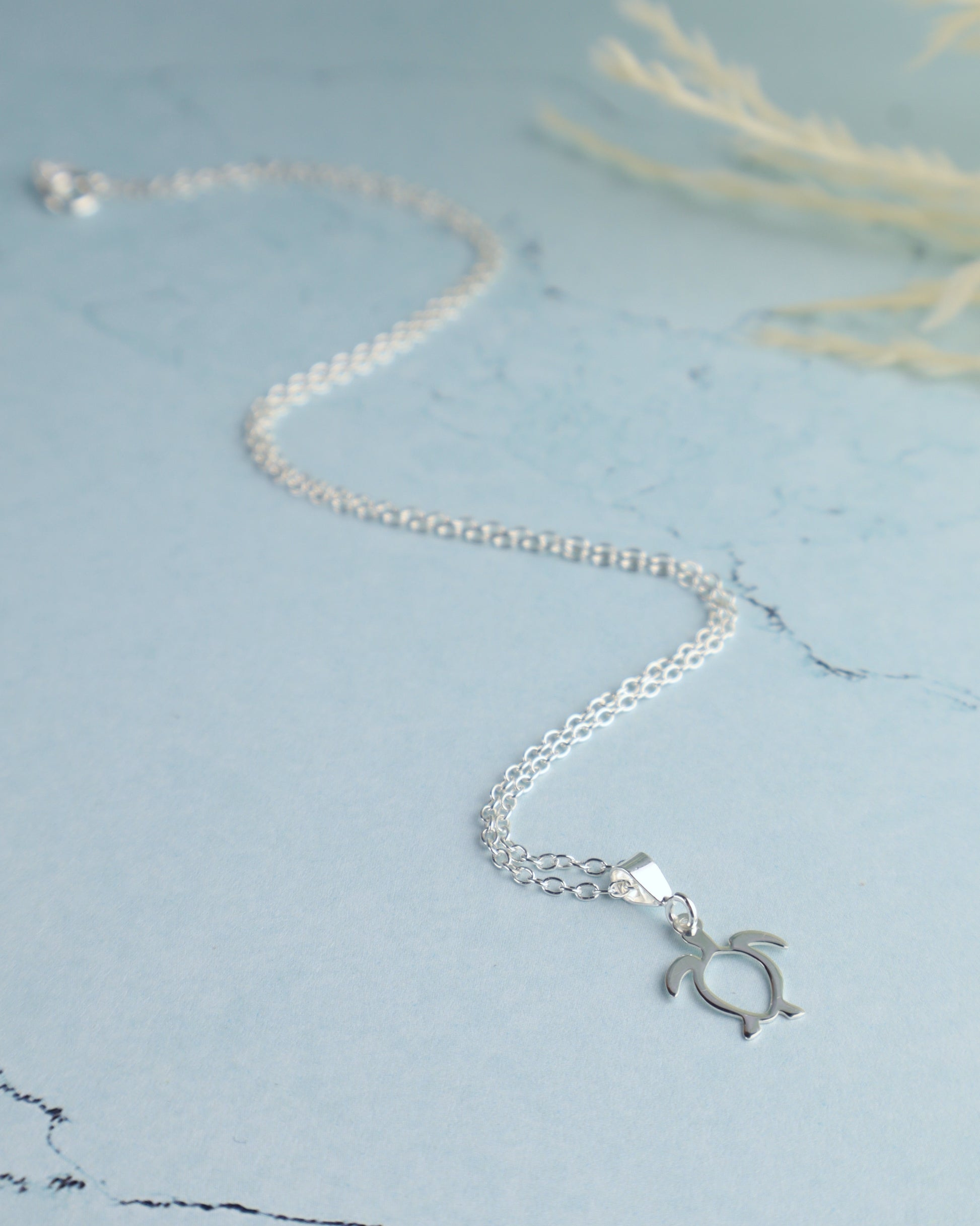 sterling silver sea turtle necklace for women resting on a blue background