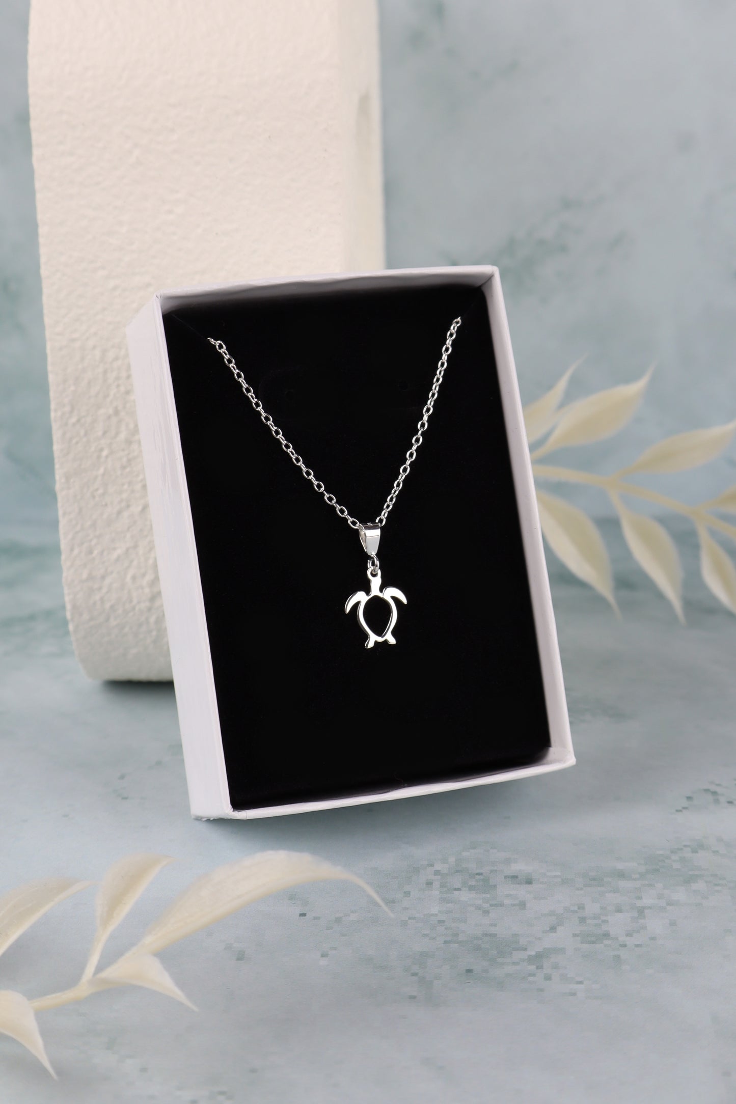 sterling silver sea turtle necklace for women in a white box placed on a black insert